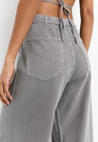 Grau weite Hosen mit einem Kordelzugbund, ausgestattet mit zwei Gesäßtaschen und einem dezenten strukturierten Stoff.