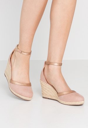 Sandały na koturnie w kolorze różowego beżu z falistymi, brązowymi paskami i plecionymi obcasami z juty. Regulowany pasek wokół kostki z ozdobną złotą klamrą.