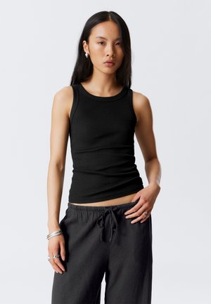 Zwart geribbeld tanktop met een ronde hals en mouwloze stijl. Gecombineerd met losse zwarte broek. Glad textuur, slanke pasvorm.