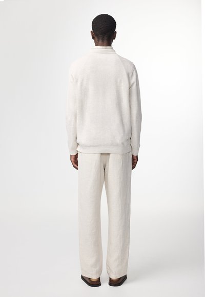 Lys beige sweater med en struktureret mønster, der har krave og ribbede manchetter, parret med matchende lyse beige bukser.