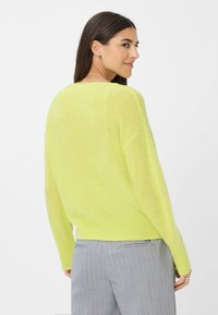 Leichter, übergroßer Pullover in leuchtend gelbgrün, mit strukturiertem Strick, lässigen Schultern und geripptem Saum. Kombiniert mit grauen gestreiften Hosen.