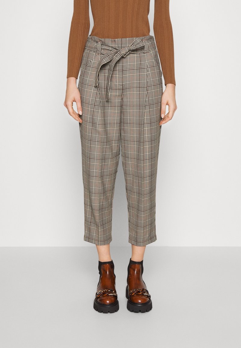 Femme portant un pantalon court beige à carreaux taille haute avec une ceinture nouée, un pull côtelé marron et des bottines en cuir marron avec un détail chaîne.