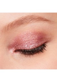 Ombre à paupières rose scintillant appliquée sur la paupière, mettant en valeur une finition texturée ; de longs cils noirs encadrent l'œil.