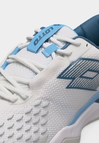 Λευκό και ανοιχτό μπλε αθλητικό παπούτσι Lotto με υφασμάτινο επάνω μέρος με υφή και λογότυπο στη πλευρά, εμφανίζοντας κοντινή εικόνα στα κορδόνια και την περιοχή της γλώσσας.