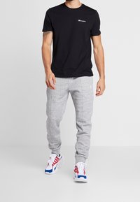 Black cotton t-shirt with a small white logo, paired with grey sweatpants featuring side seams. Footwear has red, white, and blue accents.