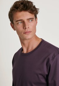 Chemise à manches longues de couleur violet foncé en tissu lisse, dotée d'un col rond côtelé et d'une coupe décontractée. Design simple et minimaliste.