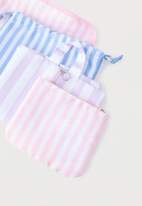 Τρεις υφασμάτινες θήκες με ρίγες σε ροζ, μοβ και μπλε χρώμα, με φερμουάρ και μικρή λαβή, τοποθετημένες η μία πάνω στην άλλη σε λευκό φόντο.