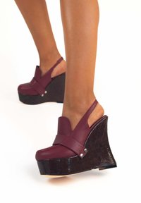 Sandali con zeppa in pelle borgogna, con retro aperto, ampia fascia anteriore e piattaforma in legno scuro texturizzato.