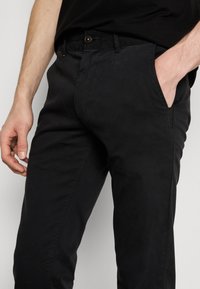 Black cotton trousers with a smooth texture, slim-fit design, front pockets, and a button closure at the waistband.