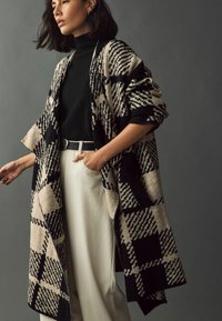 Uldblandet cardigan med et sort og beige ternet mønster. Har en løs pasform, brede ærmer og forlommer, som er parret med en sort rullekrave.