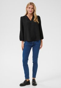 Black, V-neck blouse with long puffed sleeves, paired with blue jeans and black loafers. Smooth texture, relaxed fit, minimal detailing.