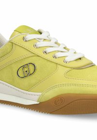 Baskets en daim jaune et cuir avec lacets blancs, logo métallique sur le côté, et semelle en caoutchouc marron texturée.