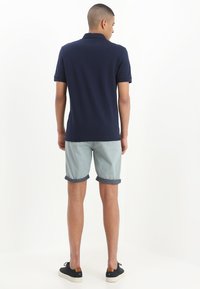 Marinblå pikétröja med korta ärmar, tillsammans med ljusblå shorts. Shortsen har uppvikta fållar och är stylade med svarta sneakers.