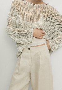 Crème-kleurige gebreide trui met een losse, open weefstructuur en ruime mouwen, gecombineerd met lichtbeige hoge taille broek.