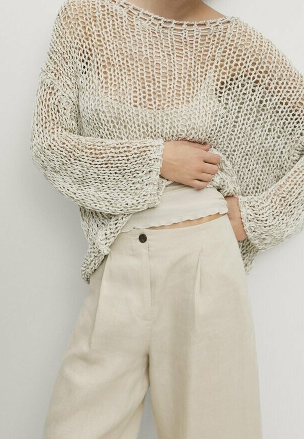 Crème-kleurige gebreide trui met een losse, open weefstructuur en ruime mouwen, gecombineerd met lichtbeige hoge taille broek.