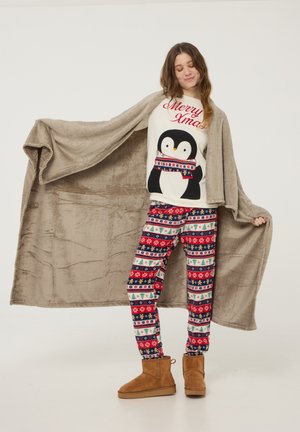 Coprente coperta in morbido pile color marrone chiaro, abbinata a una maglietta crema con una grafica di pinguino e testo festivo rosso, e pantaloni rossi con motivi di alberi e fiocchi di neve.