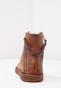 Hnědá kožená kotníčková bota s hladkým povrchem, bočními zipy a malým poutkem na zadní straně. Pevná podrážka s přirozenou texturou.