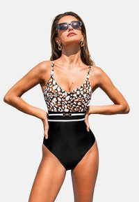 Zwarte eendelige badpak met een patroon op de bustier in oranje en wit, dunne bandjes en een contrasterende tailleband met een gouden accent.