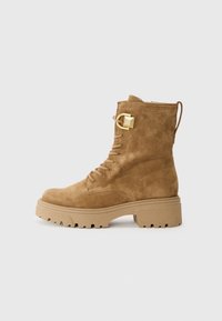 Bruine suède enkellaars met een robuuste rubberen zool, vetersluiting en goudkleurige hardwaredetails. Heeft een aantrek lus aan de achterkant.