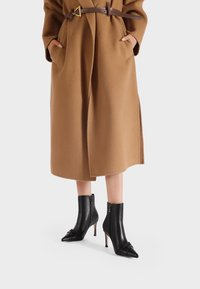 Stivali ankle in pelle nera con punte affusolate e dettagli decorativi a nodo, dotati di un alto tacco a stiletto e cerniere laterali.