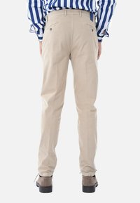 Pantaloni beige con taglio dritto, due tasche posteriori con chiusura a bottone e polsini elasticizzati, abbinati a stivali grigi.