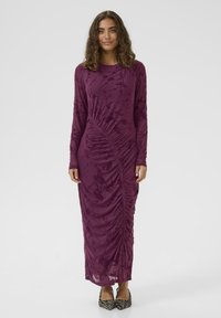 Långärmad, lila klänning med rynkdetaill och blommönster. Tillverkad av mjukt tyg, med maxi-längd och en figurnära form.