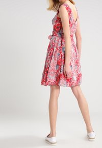 Rotes Blumenkleid mit tailliertem Oberteil, schwingendem Rock und einem Bindegürtel. Verfügt über einen V-Rücken und Kurzärmel, mit aufwendigen Paisley-Mustern.