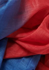 Tejido ligero y transparente en vibrantes tonos de azul y rojo, con un acabado suave y texturizado, dispuesto en pliegues fluidos. No hay patrones ni elementos de sujeción visibles.