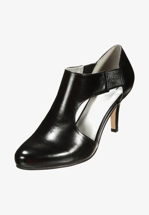 Bottine en cuir noir avec une découpe en peekaboo, un bout pointu élégant et un talon fin à hauteur de jambe. L'intérieur présente un revêtement argenté brillant.