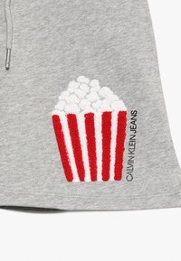 Szara bluza z teksturowanym wzorem popcornu w białe i czerwone paski, z napisem „CALVIN KLEIN JEANS” obok grafiki.