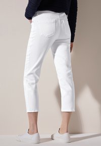 Jeans blancos cortos de mezclilla, con un diseño ajustado, dobladillos enrollados y bolsillos traseros. Combinados con zapatillas blancas sobre un fondo neutro.