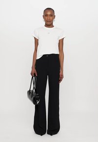 White short-sleeve t-shirt with a small printed logo, paired with high-waisted black wide-leg trousers. Holding a black handbag.