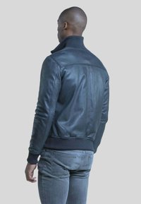 Zwarte leren bomberjack met geribbelde kraag en manchetten, met een strakke uitstraling en een soepele textuur. Gedragen over grijze jeans.