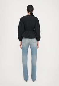 Svart, teksturert topp med pufferm og tettsittende midje, sammen med lyseblå, høyhåndtaks rette jeans.
