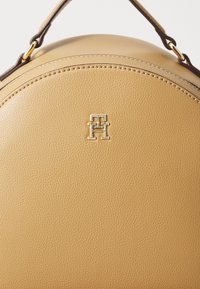 Runde, braune Lederhandtasche mit strukturierter Oberfläche, ausgestattet mit goldfarbenen Beschlägen und einem auffälligen Logodesign.