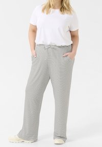 T-shirt blanc ample associé à un pantalon large rayé noir et blanc, avec une taille à cordon et des poches latérales.