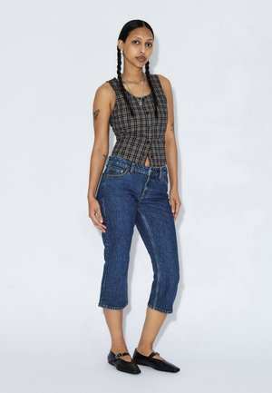 Czarna i biała kraciasta bluzka bez rękawów z wcięciem w talii, zestawiona z niebieskimi jeansami o długości 7/8 oraz czarnymi balerinami z klamrą.