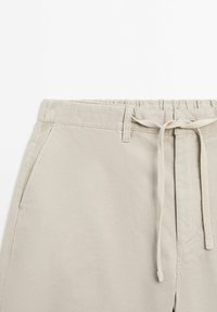 Lys beige joggerbukser med elastisk talje, snøre-lukning, to sidelommer og en glat bomuldsblanding tekstur.