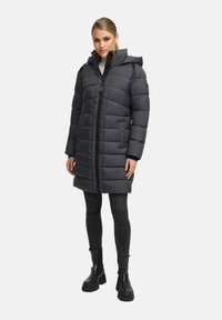 Puffer coat in dark gray, featuring a zip closure, hood, and horizontal quilted pattern. Worn with black pants and chunky boots.