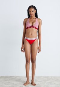 Red bikini set featuring a halter top with a textured pattern and branded waistband. The bottom has white and black horizontal stripes.