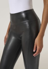 Svarta högmidjade leggings i glänsande läder. Designen har en slät textur med en åtsittande silhuett och subtila sömdetaljer.