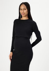 Črn, rebrast, dolg rokav, kratka majica v kombinaciji z ujemajočo se dolgo krilo. Mehak material in prilagojen dizajn poudarjata eleganten silhuet.