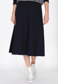 Knielanger marineblauer Strickrock mit tailliertem Bund, der sanft ausgestellt ist. Getragen mit weißen High-Top-Sneakern aus strukturiertem Stoff.