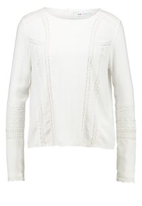 Haut blanc à manches longues avec des bordures en dentelle florale le long des épaules et des manches, doté d'un col rond et d'une texture lisse.