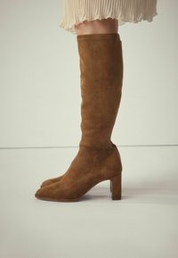 Braune Wildleder-Kniestiefel mit quadrater Zehenpartie und klobigem Absatz. Besitzt eine glatte Textur und ein nahtloses Design, geeignet für verschiedene Outfits.