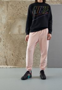 Svart sweatshirt med flerfärgad "NIKE"-logotyp, rosa sweatpants och svarta sneakers med färgglada detaljer och texturerad design.