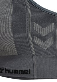 Grijze sportbeha met ribbeltextuur, voorzien van een logo en een chevronpatroon in een donkere tint. Het ontwerp is naadloos en heeft een zachte afwerking.