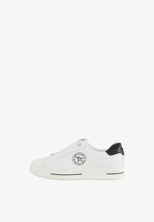 White canvas sneaker with a round toe, lace-up front, black heel accent, and circular logo detail on the side. Rubber sole with black stripe.