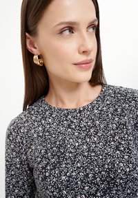 Námornícky top s kvetinovým vzorom a bielymi akcentmi, s okrúhlym výstrihom. Model má na sebe zlaté kruhové náušnice s zakriveným dizajnom. Hladká textúra.