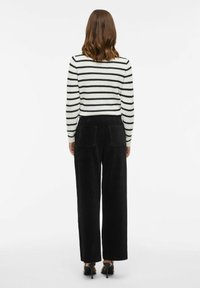 Svītrota džemperis melnbaltā krāsā, apvienots ar augsta jostas allažajā melno korduroja biksēm ar aizmugurējām kabatām un taisna griezuma kājām.